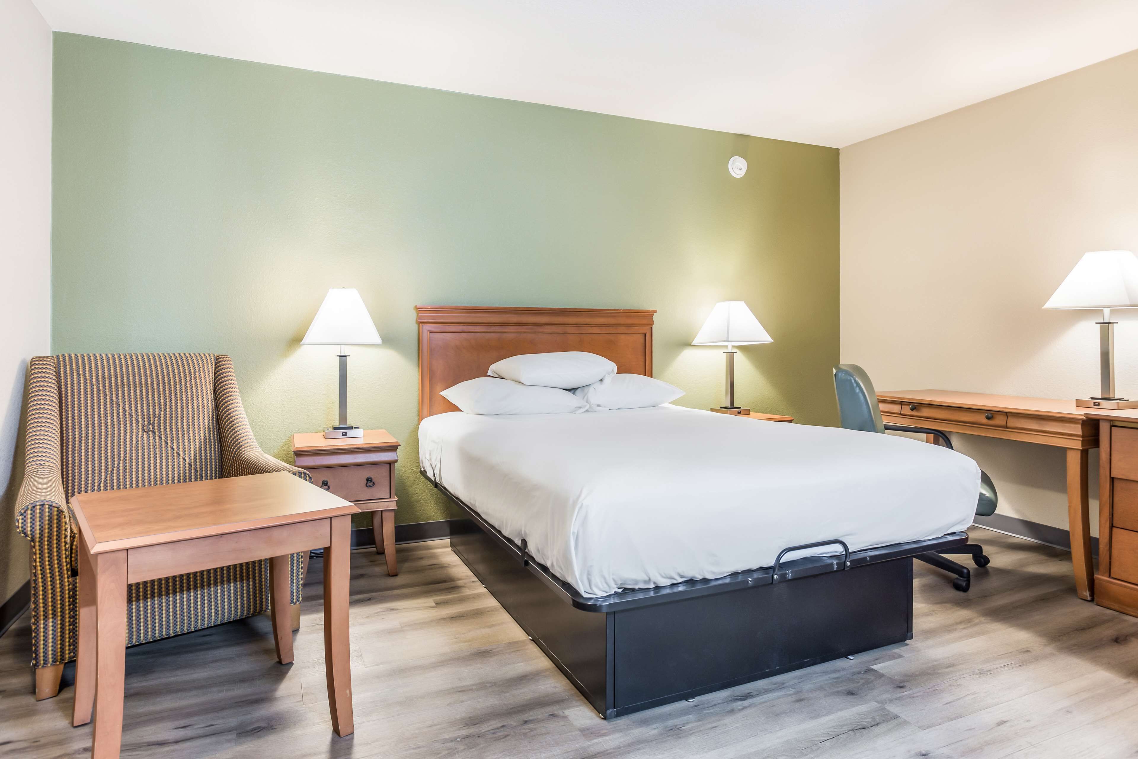 Ett hotellrum med en säng, ett skrivbord, en stol och två sänglampor.