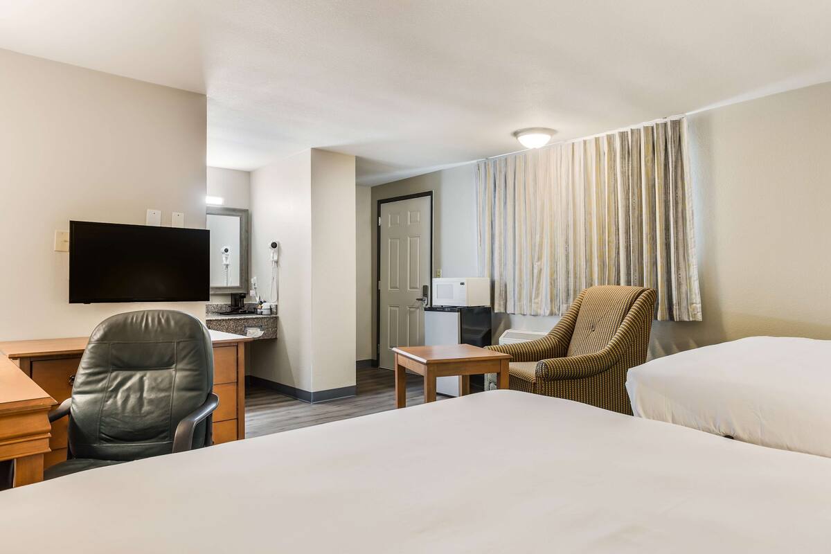 A hotel room with a bed, desk, chair, TV, and a small kitchenette.