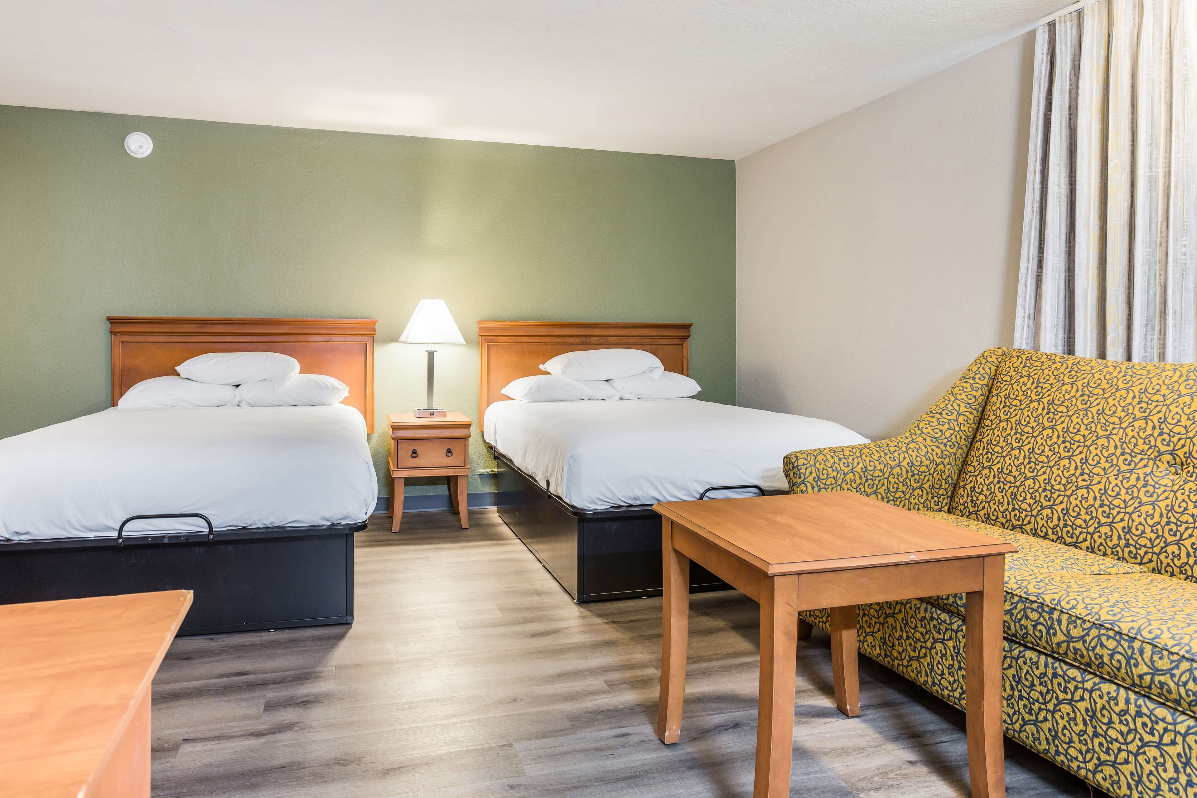 A hotel room with two beds, a sofa, a table, and a lamp.