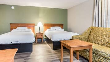 A hotel room with two beds, a sofa, a table, and a lamp.