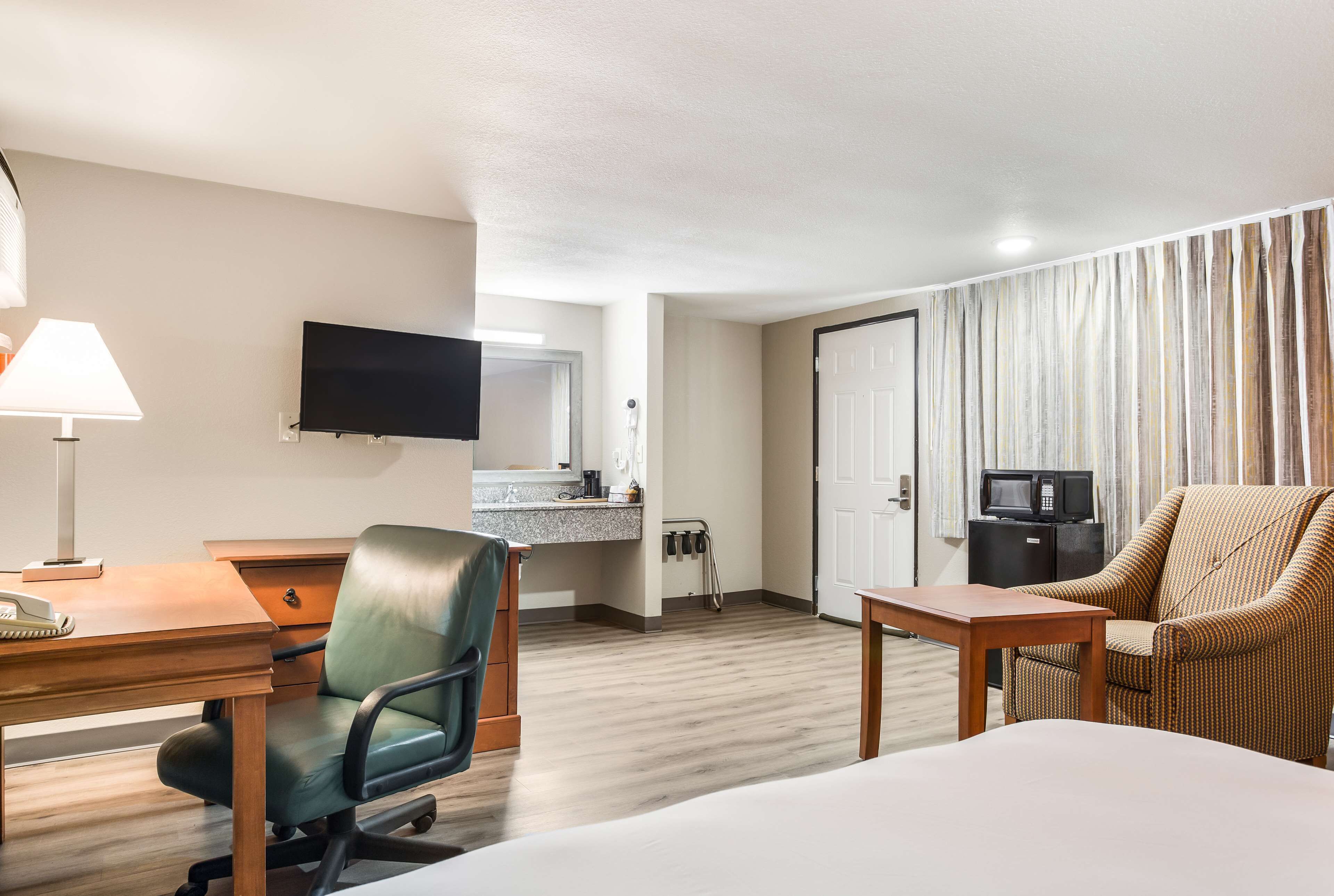 Habitación de hotel con cama, escritorio, silla, televisor y una pequeña cocina.