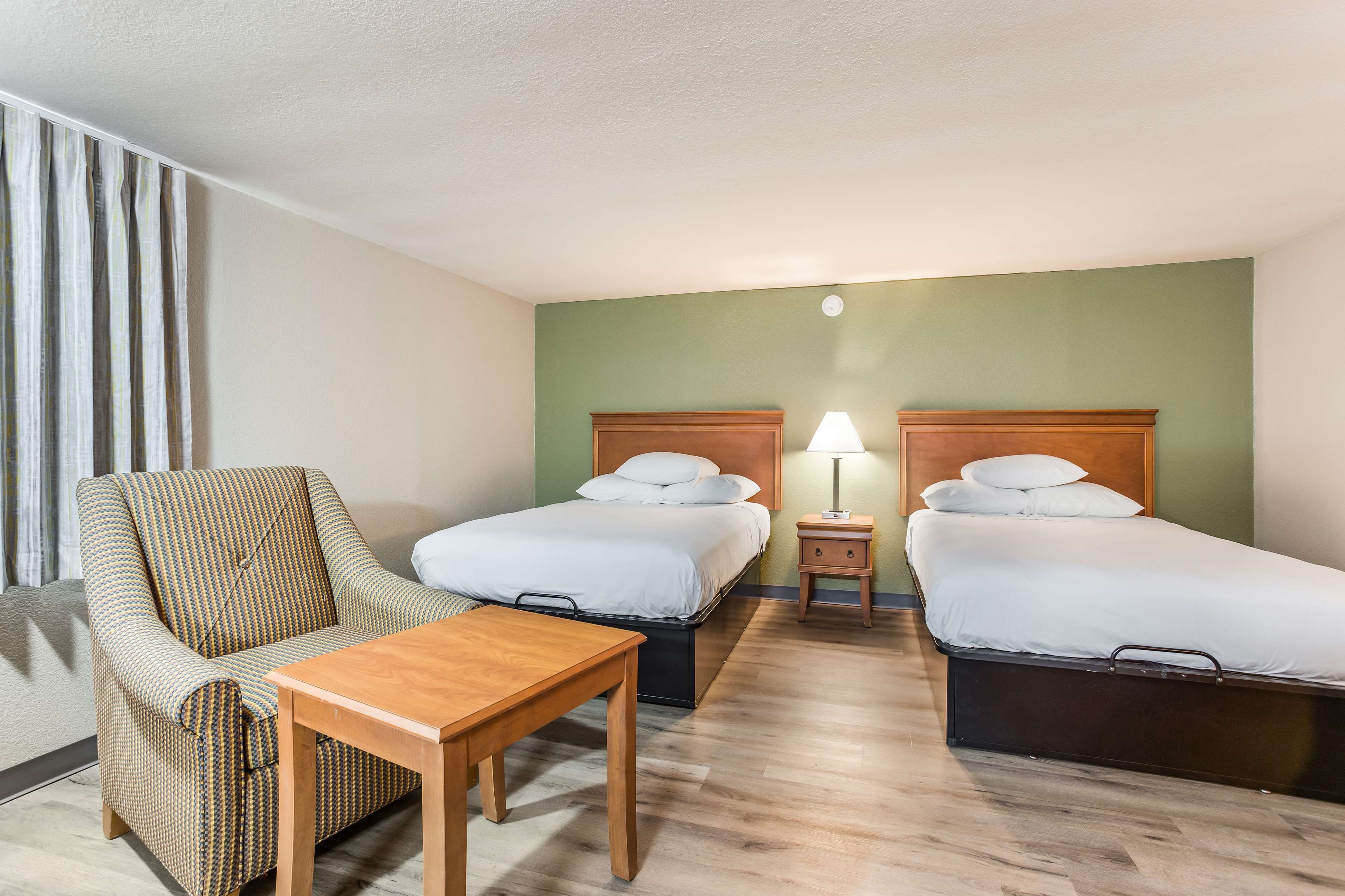 Une chambre d’hôtel avec deux lits, une chaise, une table et une lampe.