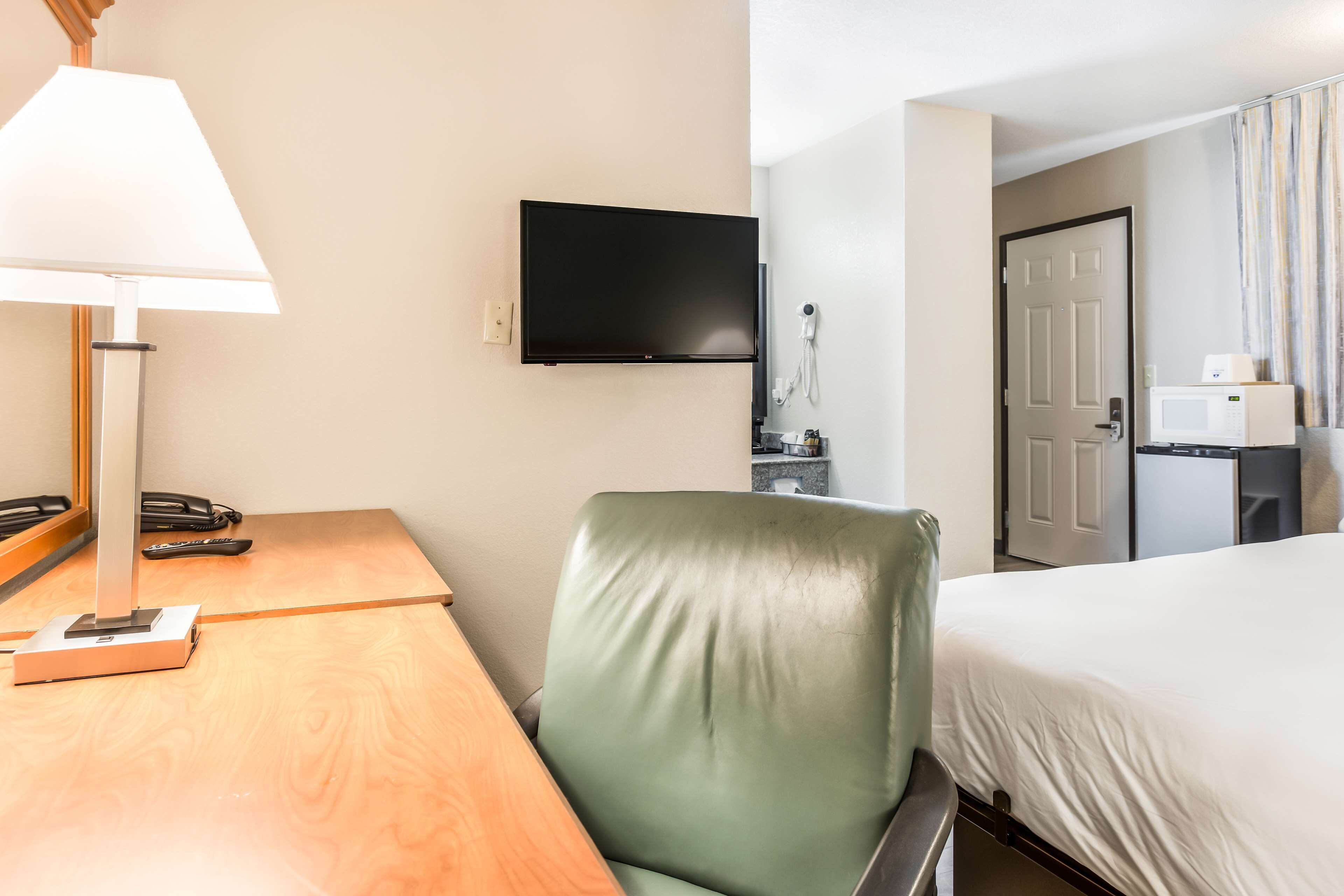 A hotel room with a bed, a desk with a lamp, a flat-screen TV, a telephone, and a microwave.