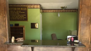 Un mostrador de recepción con un cartel que detalla las normas de la habitación, un perchero, una silla y una pequeña mesa con objetos encima.