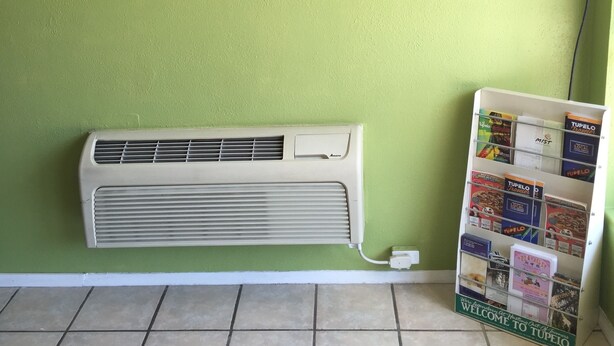 Una habitación con una pared verde, un adorno en la pared, un aire acondicionado y un cartel de bienvenida.