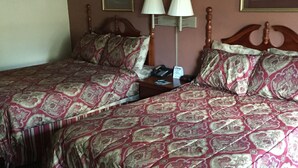 Habitación de hotel con dos camas, una mesita de noche, una lámpara y dos cuadros en la pared.