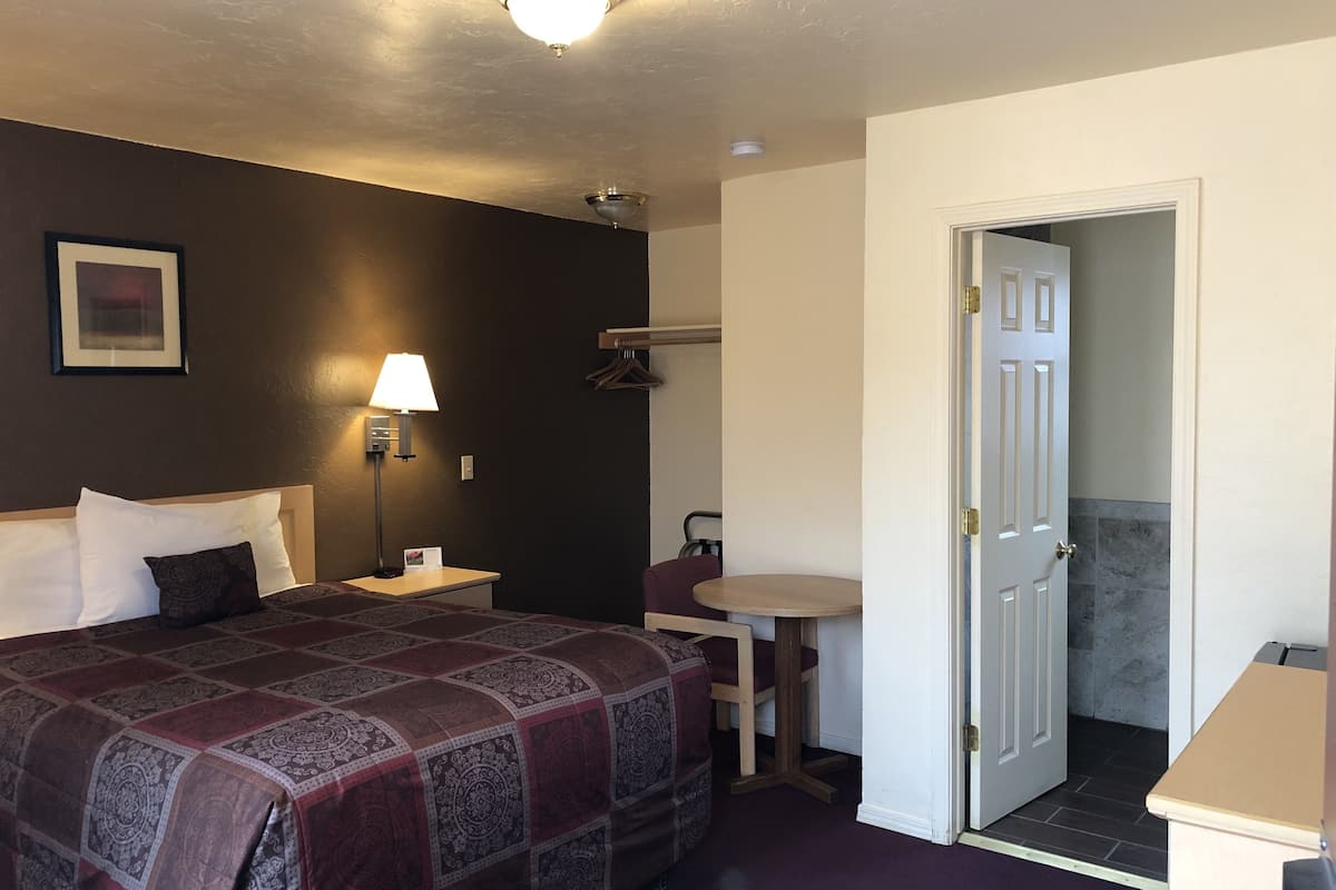 A hotel room with a bed, bedside lamp, a small table, and a door leading to a bathroom.
