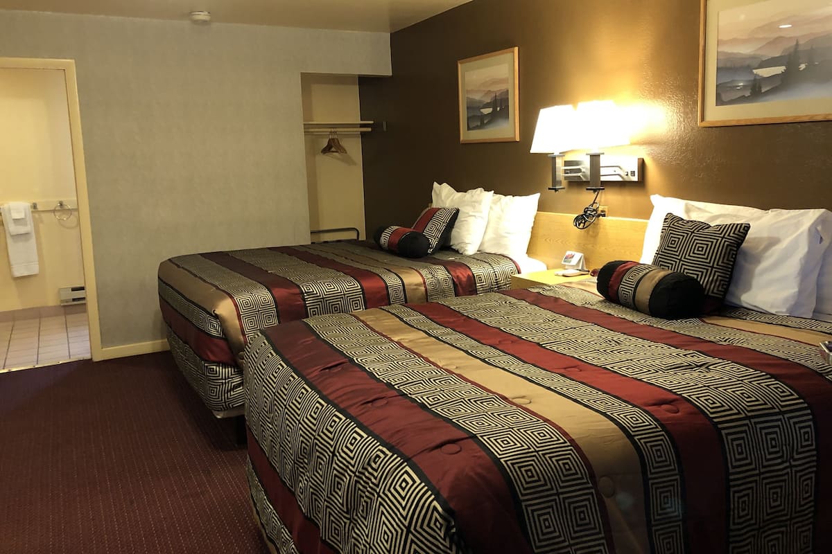 A hotel room with two beds, a nightstand, a lamp, and a painting on the wall.