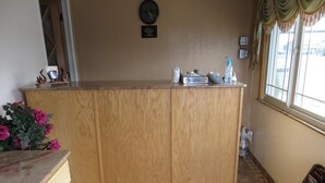 Un comptoir d’accueil en bois, avec une horloge au-dessus, une pancarte indiquant « Merci de ne pas fumer » et une fenêtre avec des rideaux.