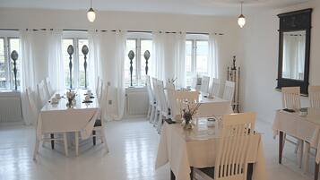 A dining area with white furniture and curtains, large windows, and a ceiling fan.