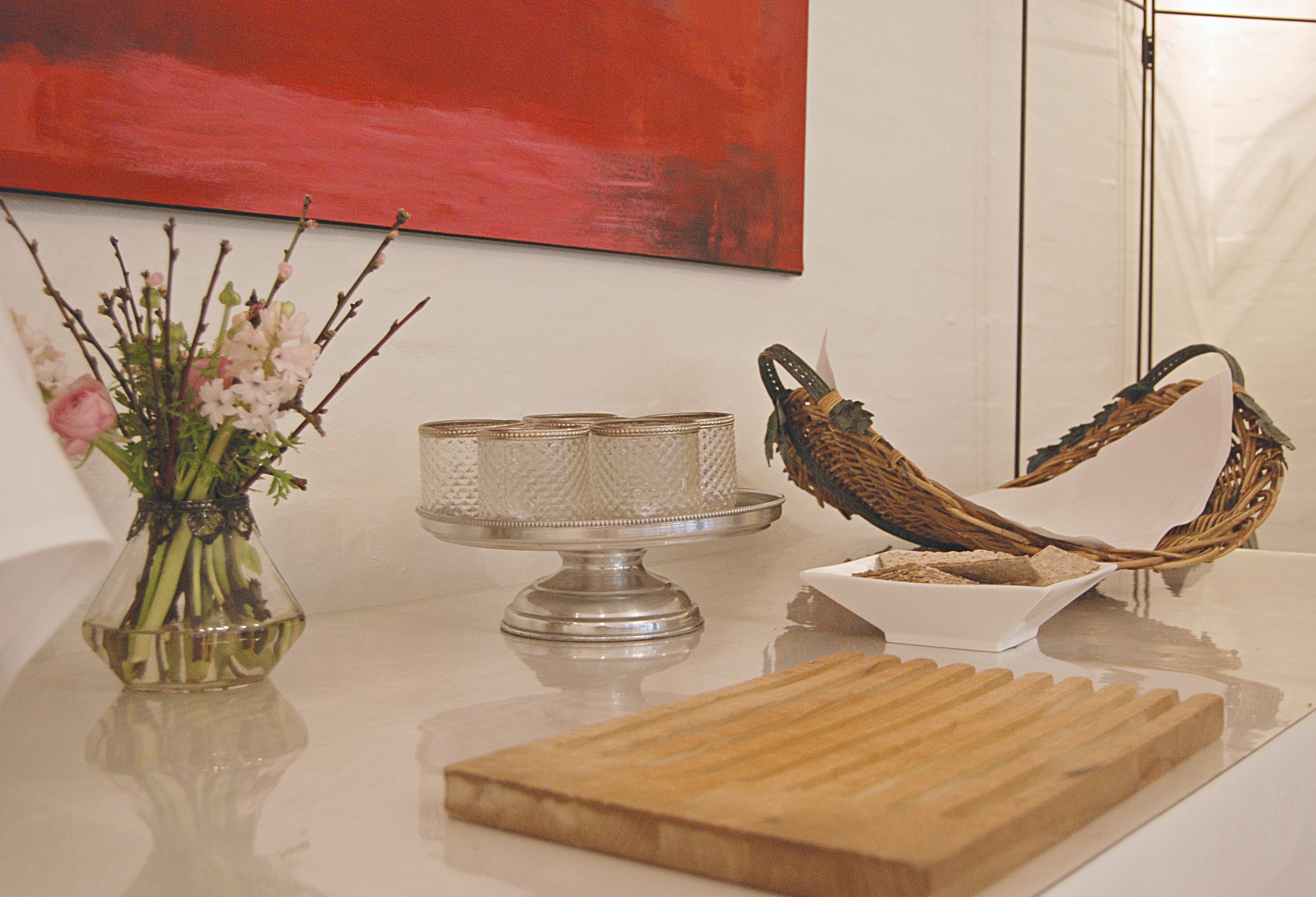 A kitchen counter with a vase of flowers, a cake stand, and a woven basket.