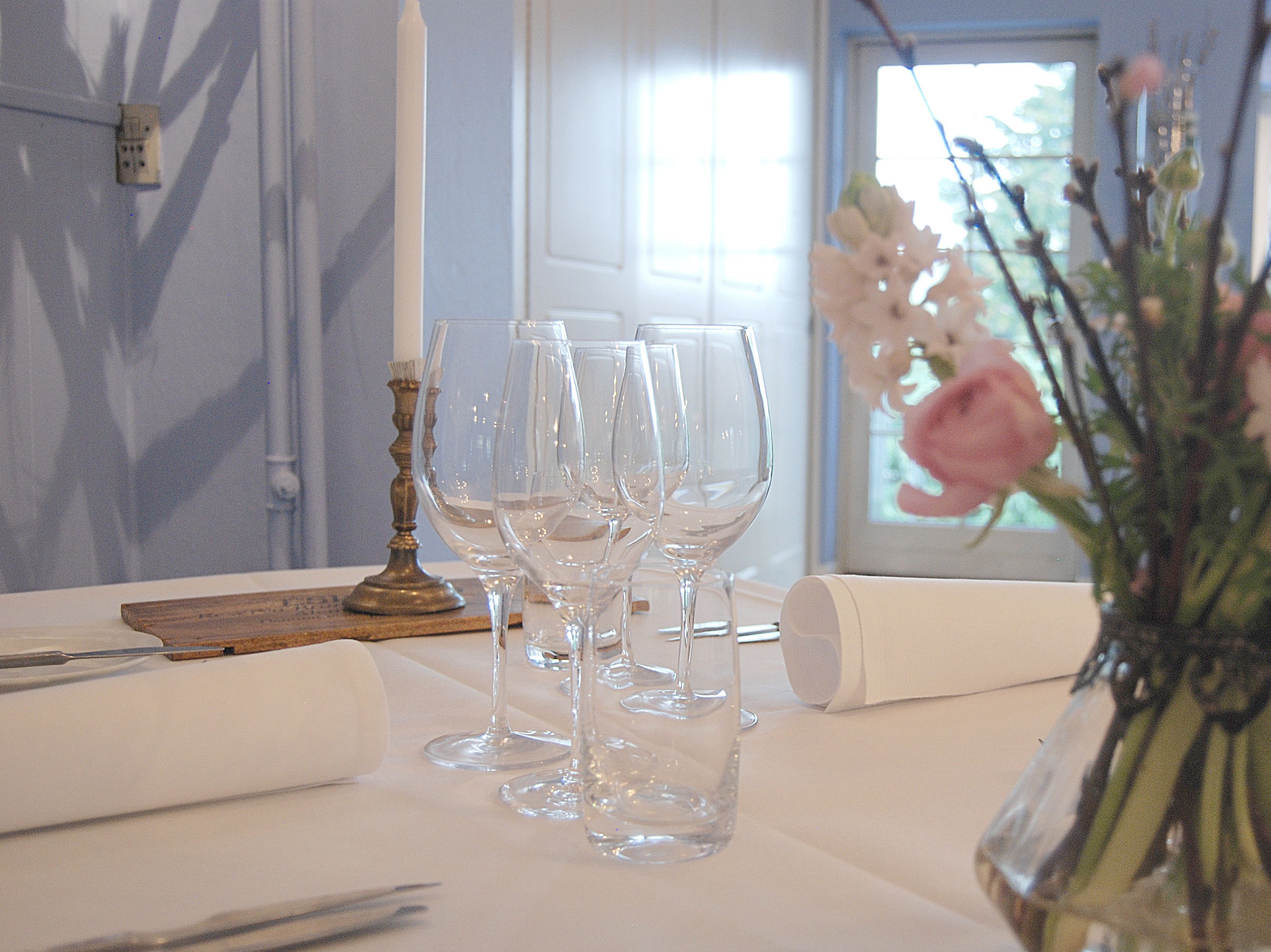 A table set with clear wine glasses, a candle holder, and a rolled napkin.