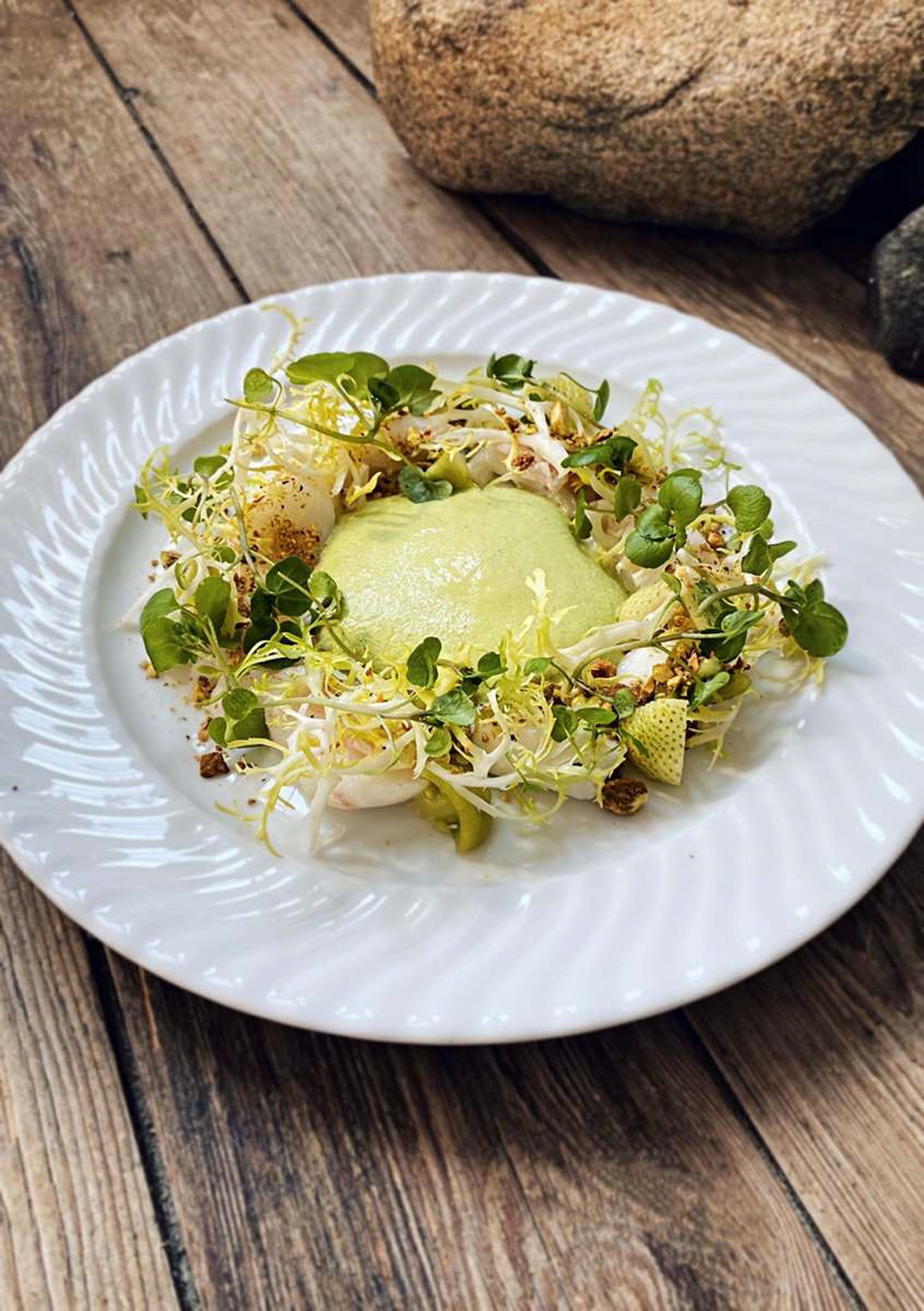 A white plate with a green sauce, sprouts, and seeds on a wooden table.