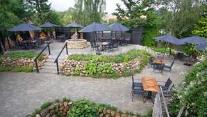 Un espace extérieur aménagé en terrasse, avec des murs en pierre, des marches en bois et plusieurs tables et chaises placées sous des parasols.