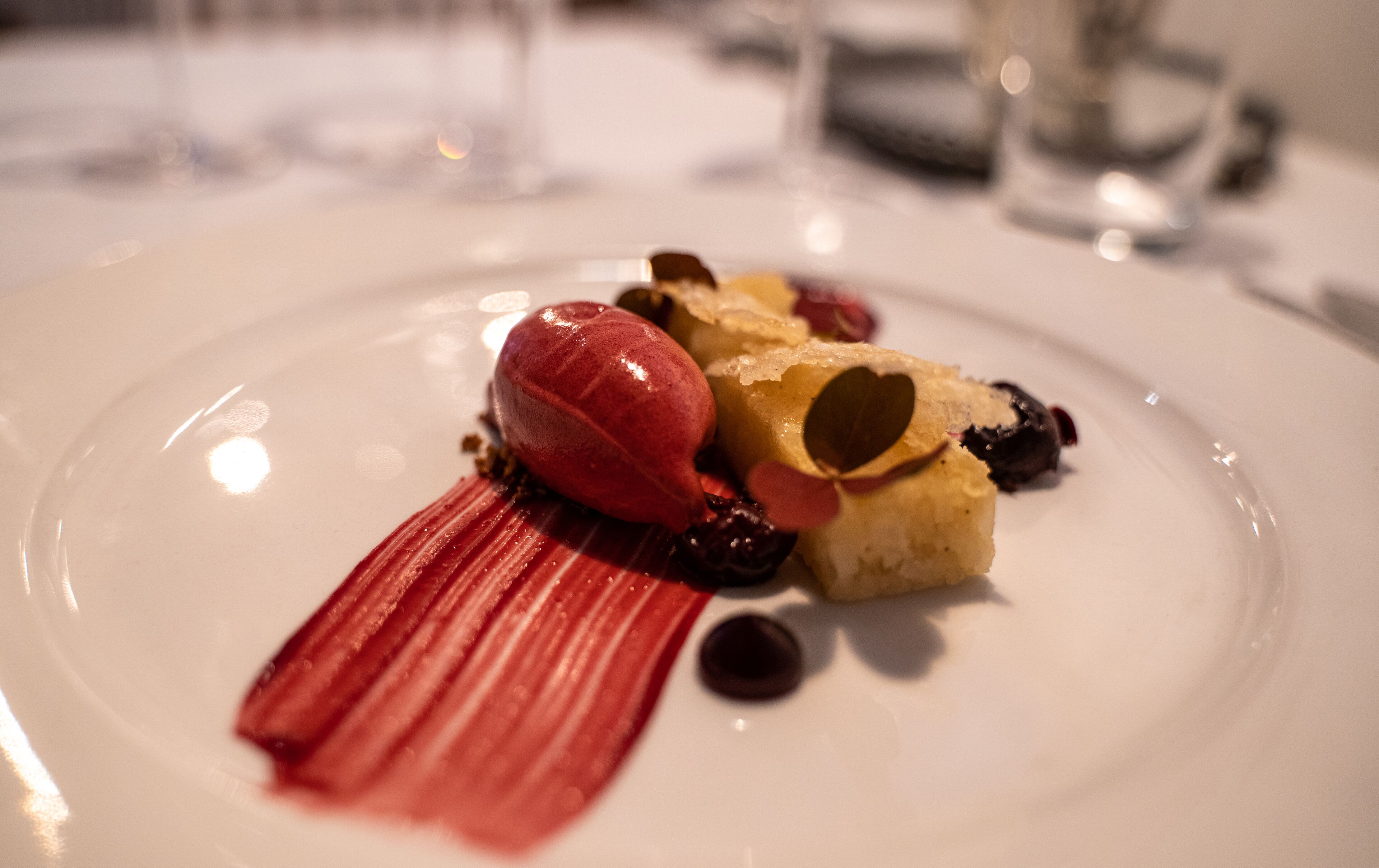 Un postre en un plato blanco con salsa roja y un elemento con forma de corazón.