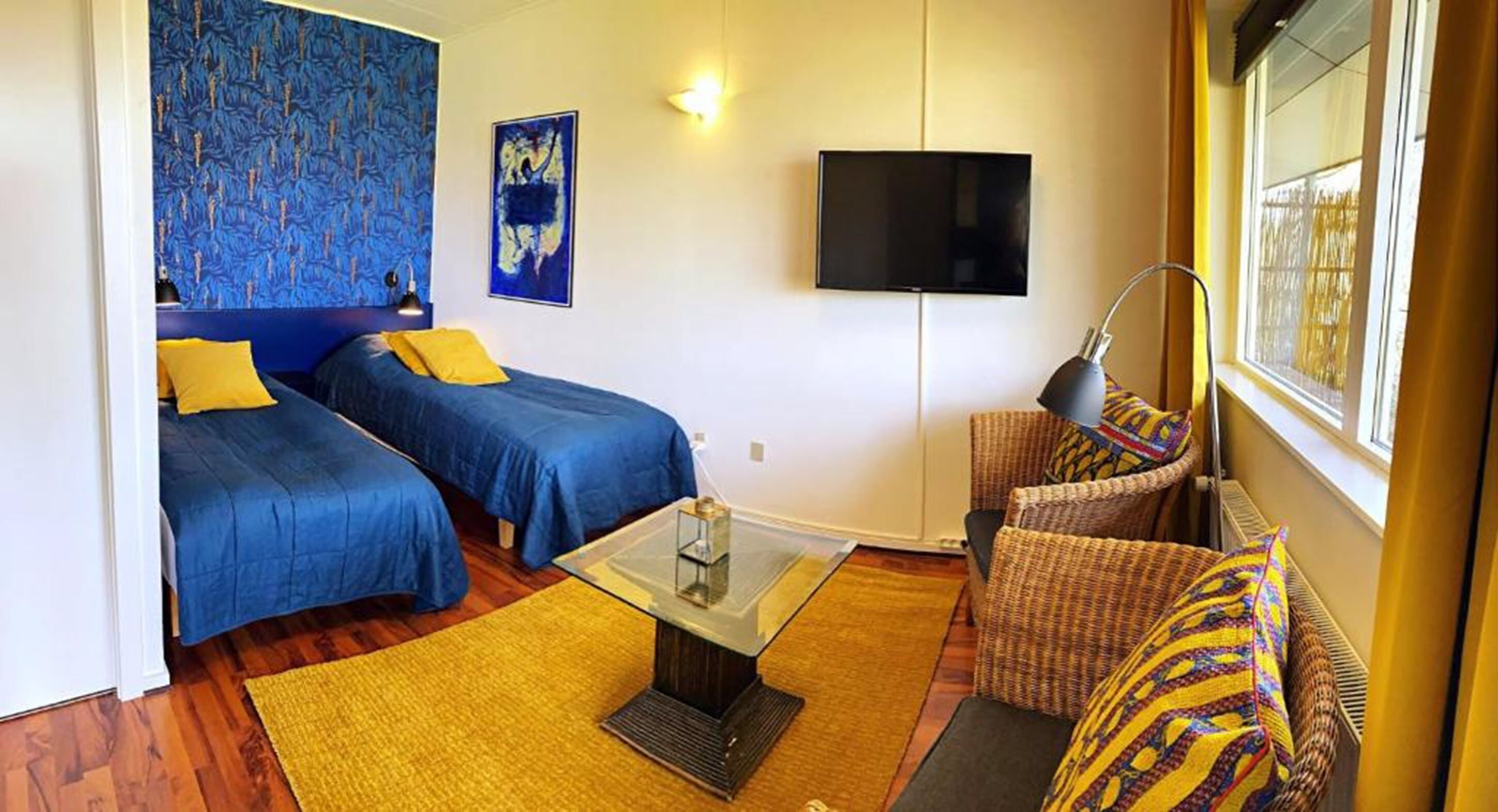 A room with two beds, a TV, and a wicker chair.