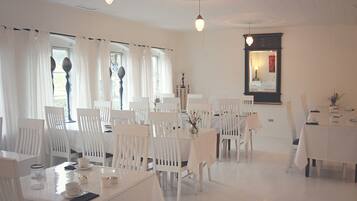 Een eetruimte met witte tafels en stoelen, een kroonluchter en een spiegel aan de muur.
