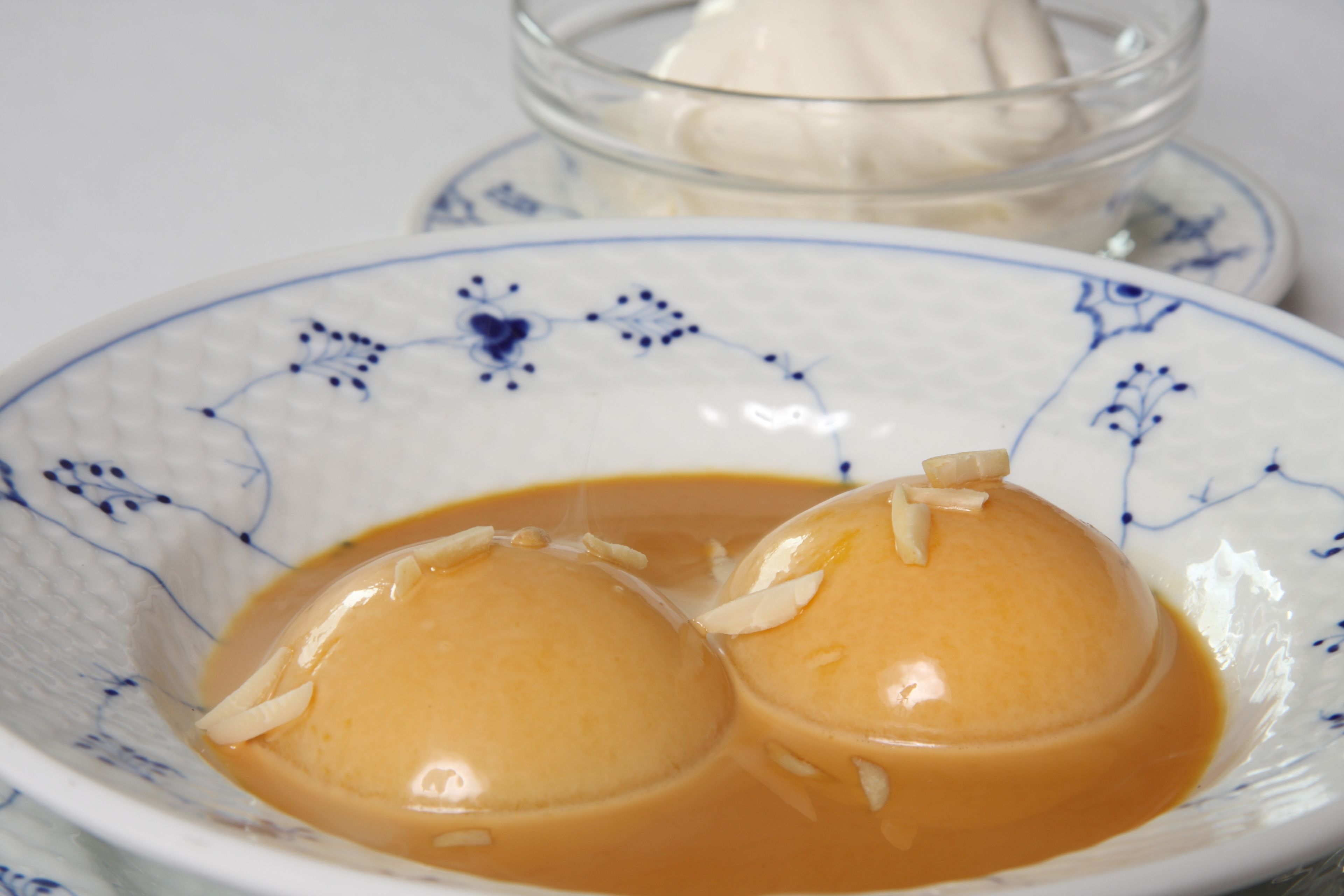 Un bol de panna cotta con salsa de caramelo y almendras, sobre un plato decorativo.