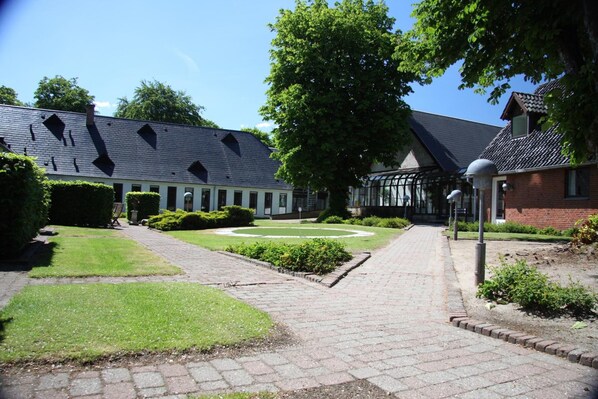 A courtyard with a paved walkway, a circular garden, and a building with a sloped roof.