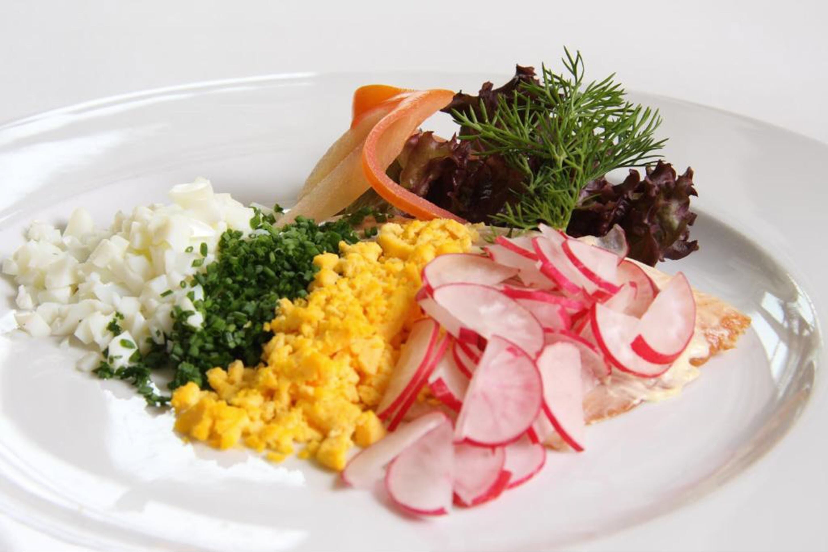A plate with scrambled eggs, diced potatoes, chopped herbs, radish slices, and a piece of salmon with dill garnish.