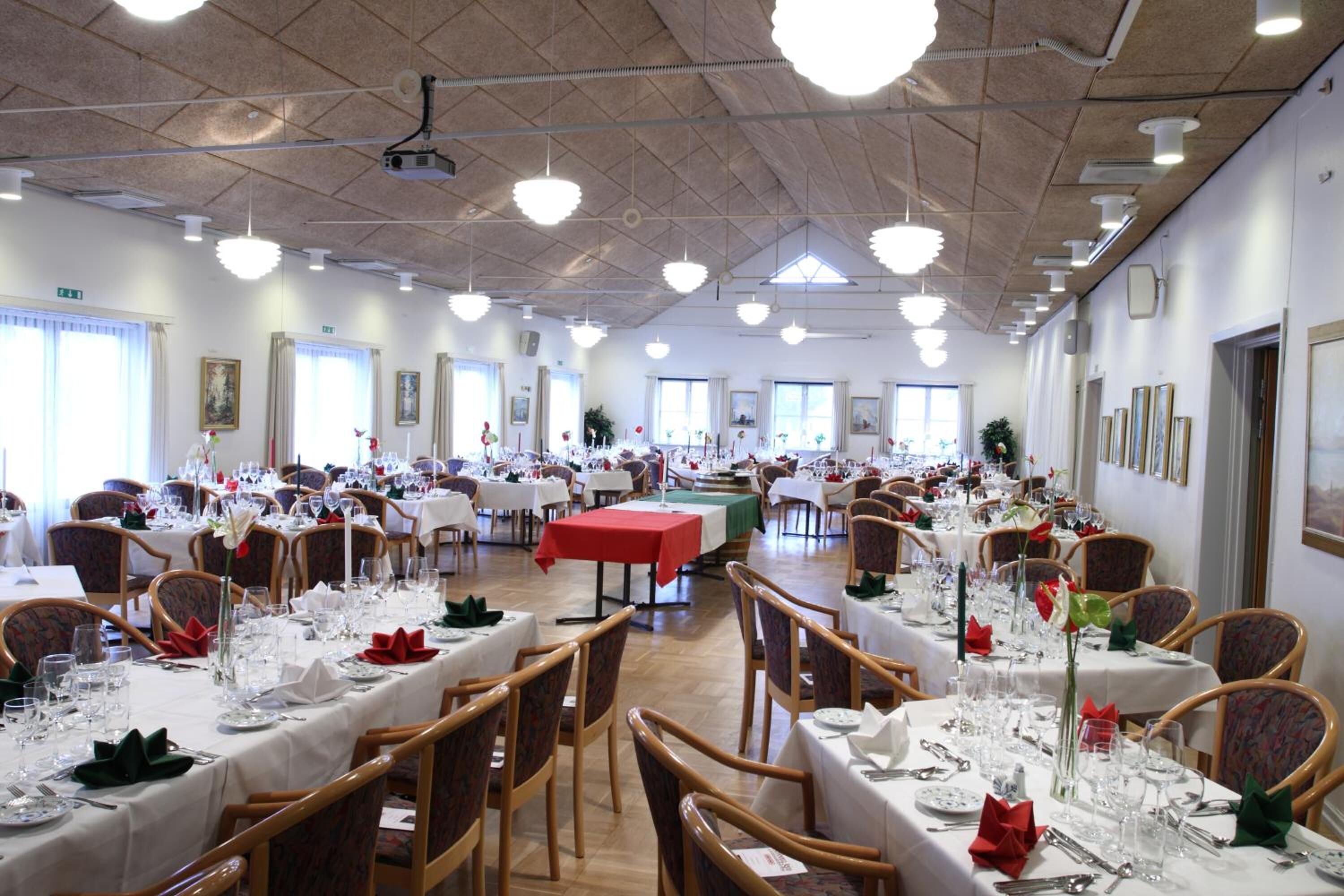 A large banquet hall with multiple tables set for dining, featuring wooden chairs and white tablecloths.