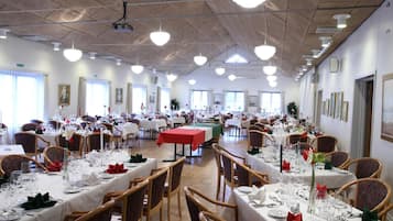 A large banquet hall with multiple tables set for dining, featuring wooden chairs and white tablecloths.