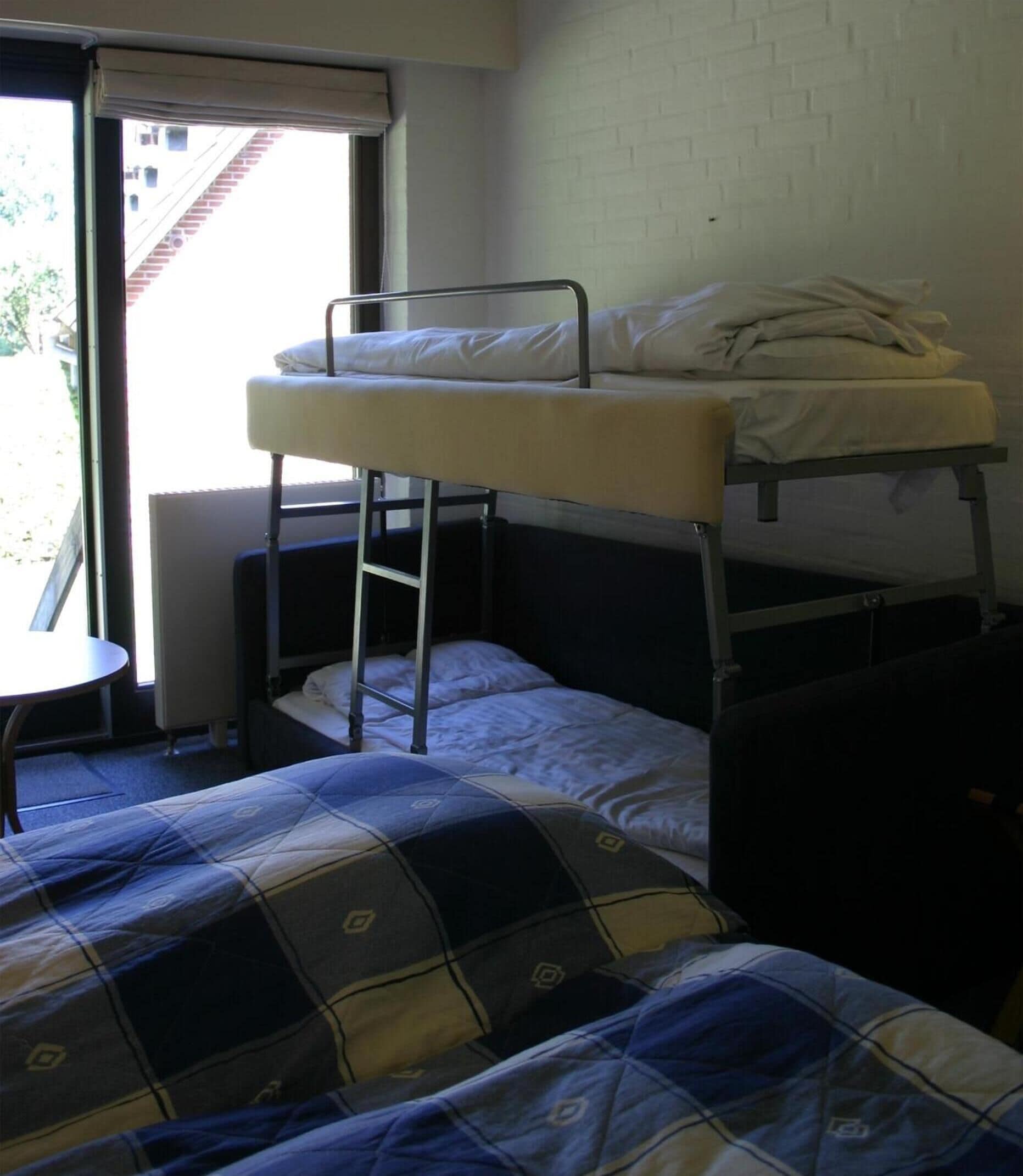 A bunk bed room with a window, a small table, and a patterned bedspread.