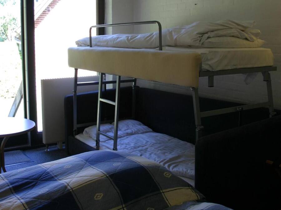 A bunk bed room with a window, a small table, and a patterned bedspread.