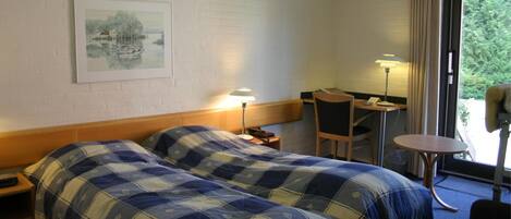 Hotelkamer met twee bedden, een bureau, een stoel, een lamp en een schilderij aan de muur.