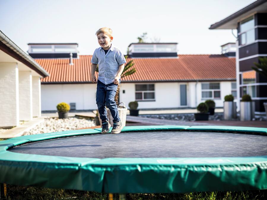 Un enfant qui saute sur un trampoline dans un quartier résidentiel, avec des maisons et un ciel dégagé.