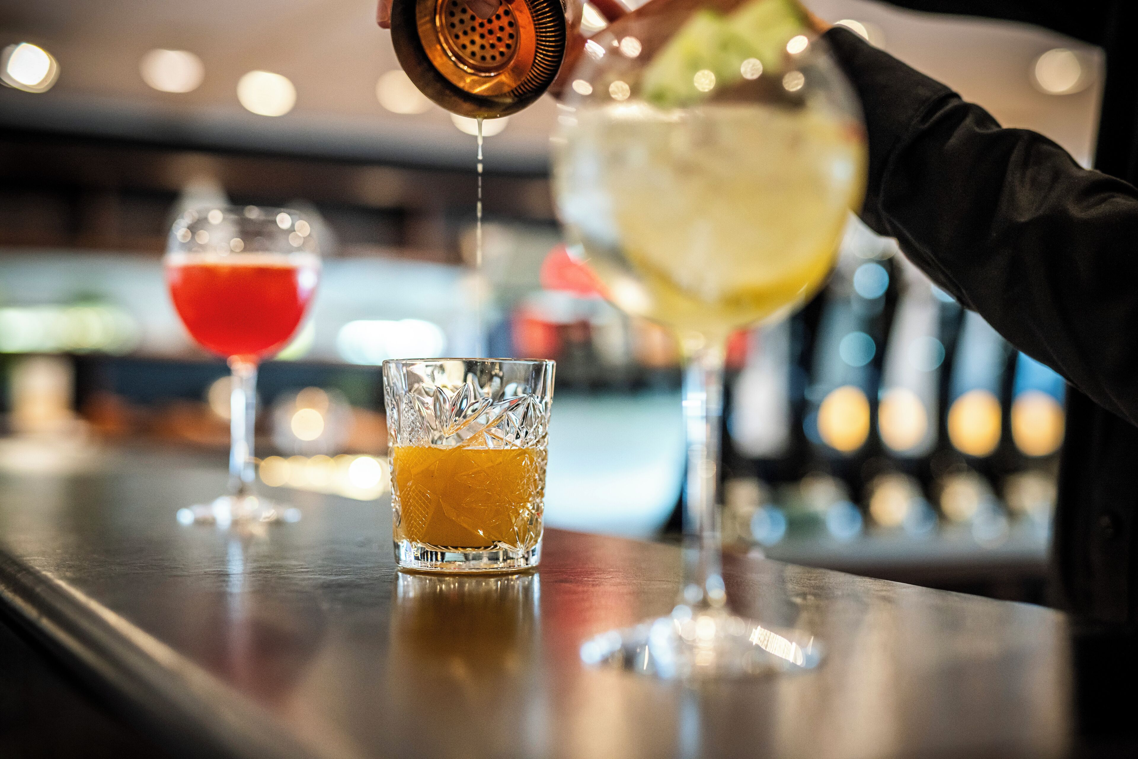 A bar setting with a person pouring a drink into a glass.