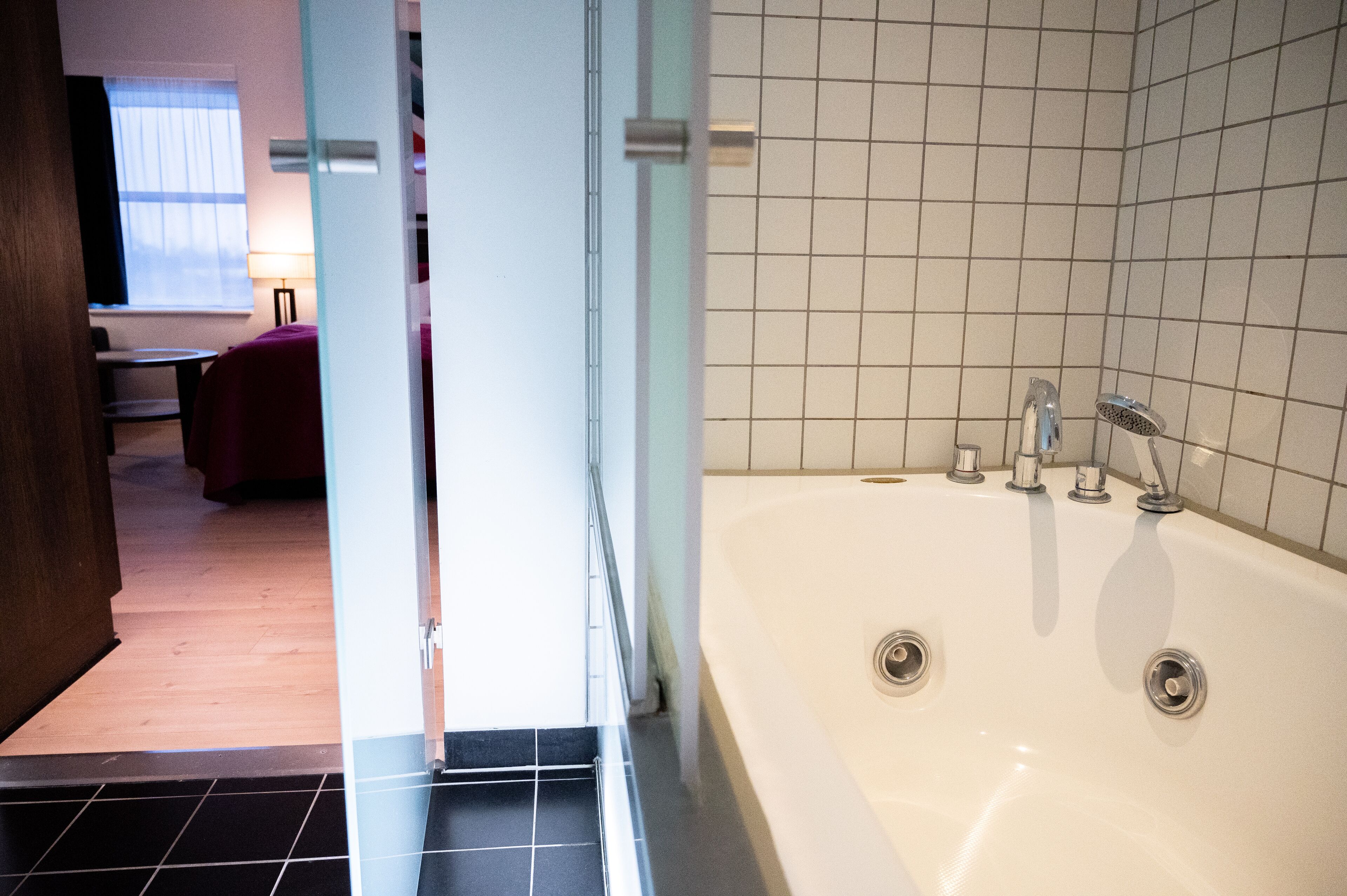 A modern bathroom with a large bathtub, tiled walls, and a visible window with curtains.