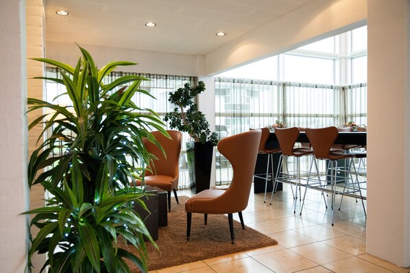 Un comedor moderno con techos altos, ventanas amplias y una variedad de disposiciones de asientos, incluyendo sillas y una mesa.