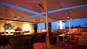 An outdoor seating area with tables and chairs under a large umbrella, a bar area with a counter, and a building in the background. - Hotel Svanen, Stays & BW Signature Collection (Billund)