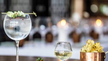 A table with a glass of water, a small dish of food, a glass of white wine, and a copper pot of chips.