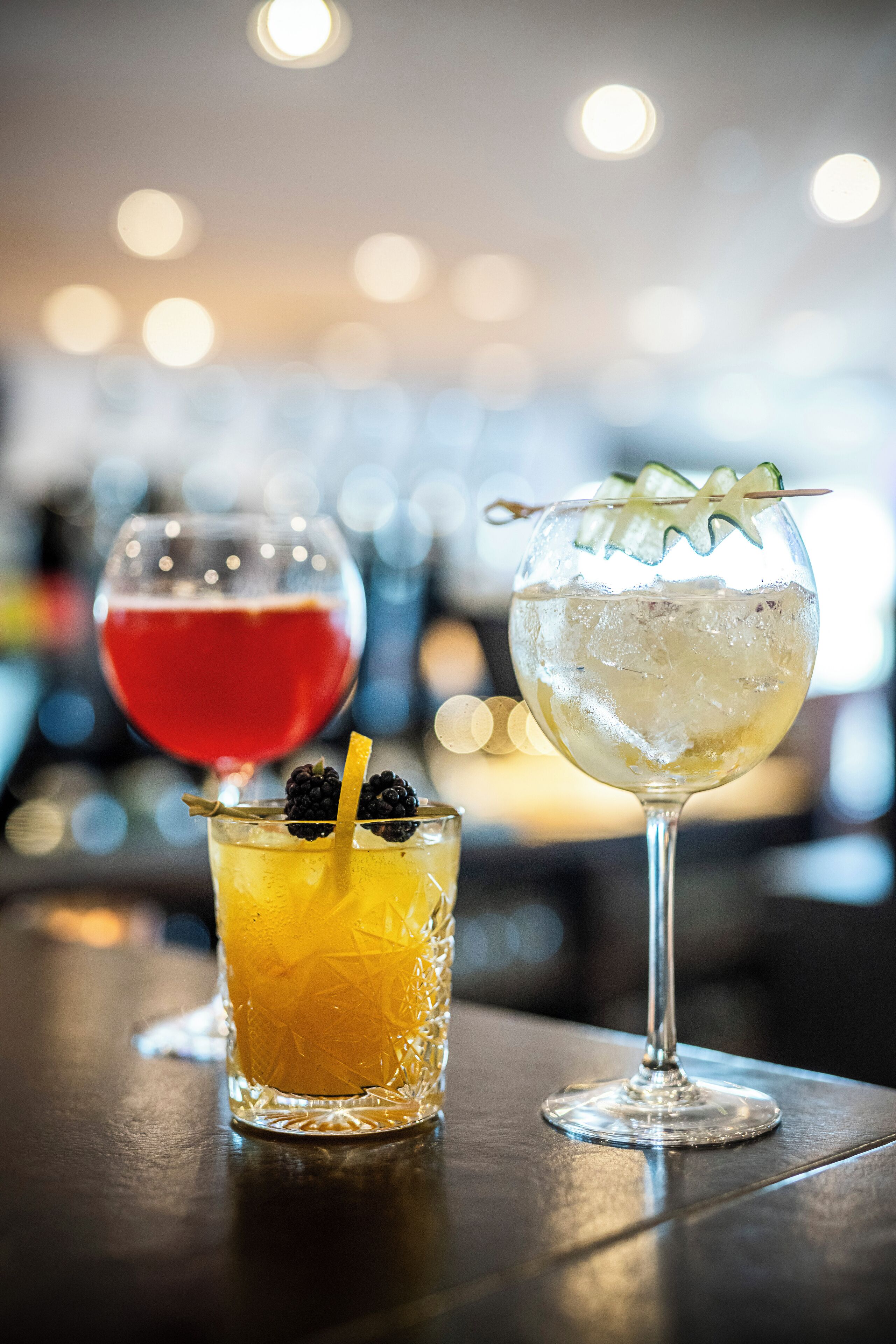 Three glasses of different beverages on a bar counter.
