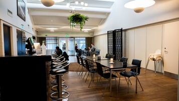 A modern conference room with a long table, black chairs, and a bar area with stools.