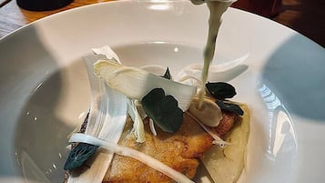 A plate with a piece of fried food, possibly chicken, topped with a creamy sauce and garnished with leaves and thinly sliced vegetables.