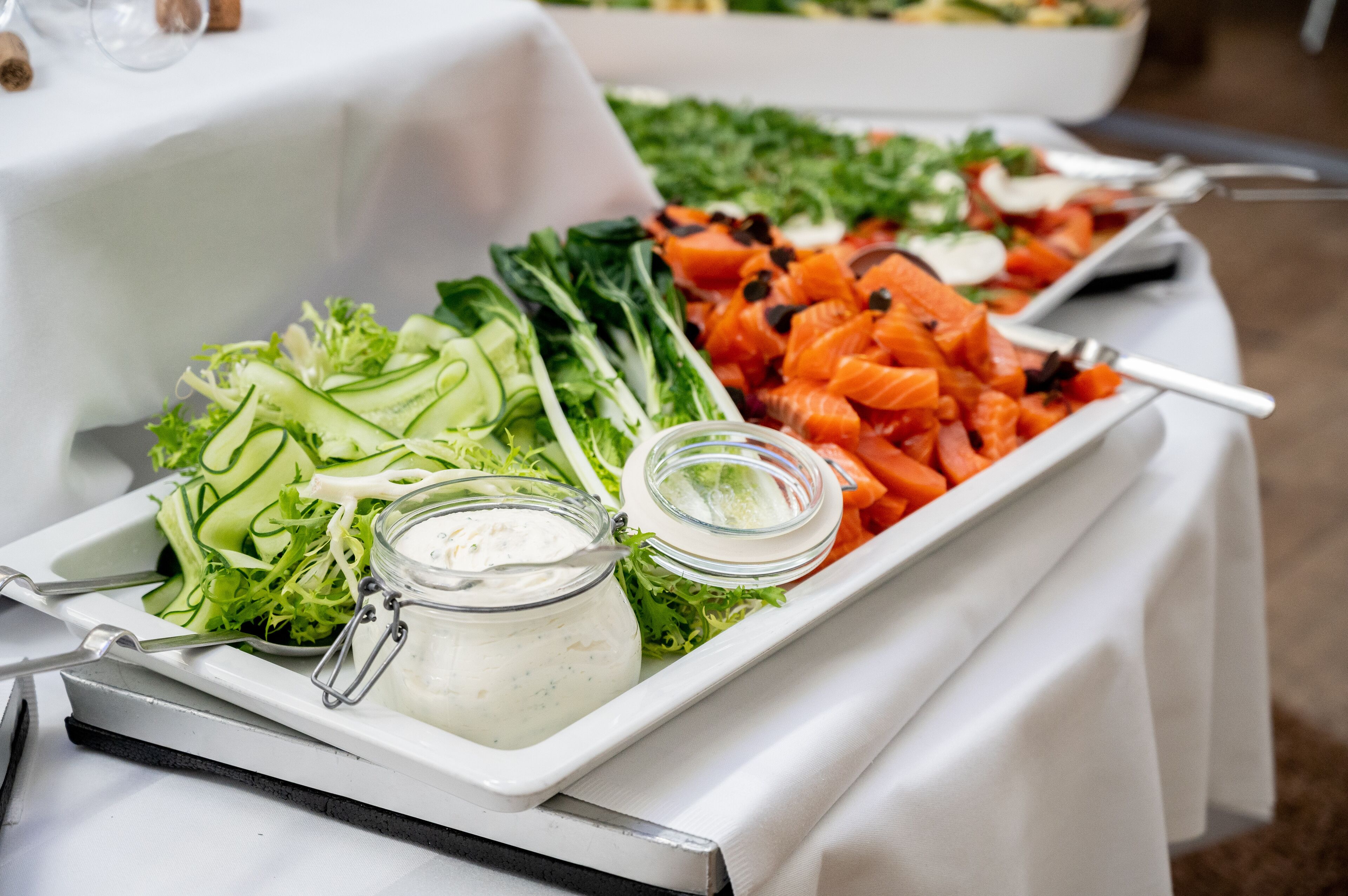 A buffet table with various food items including salads, vegetables, and a jar of dressing.