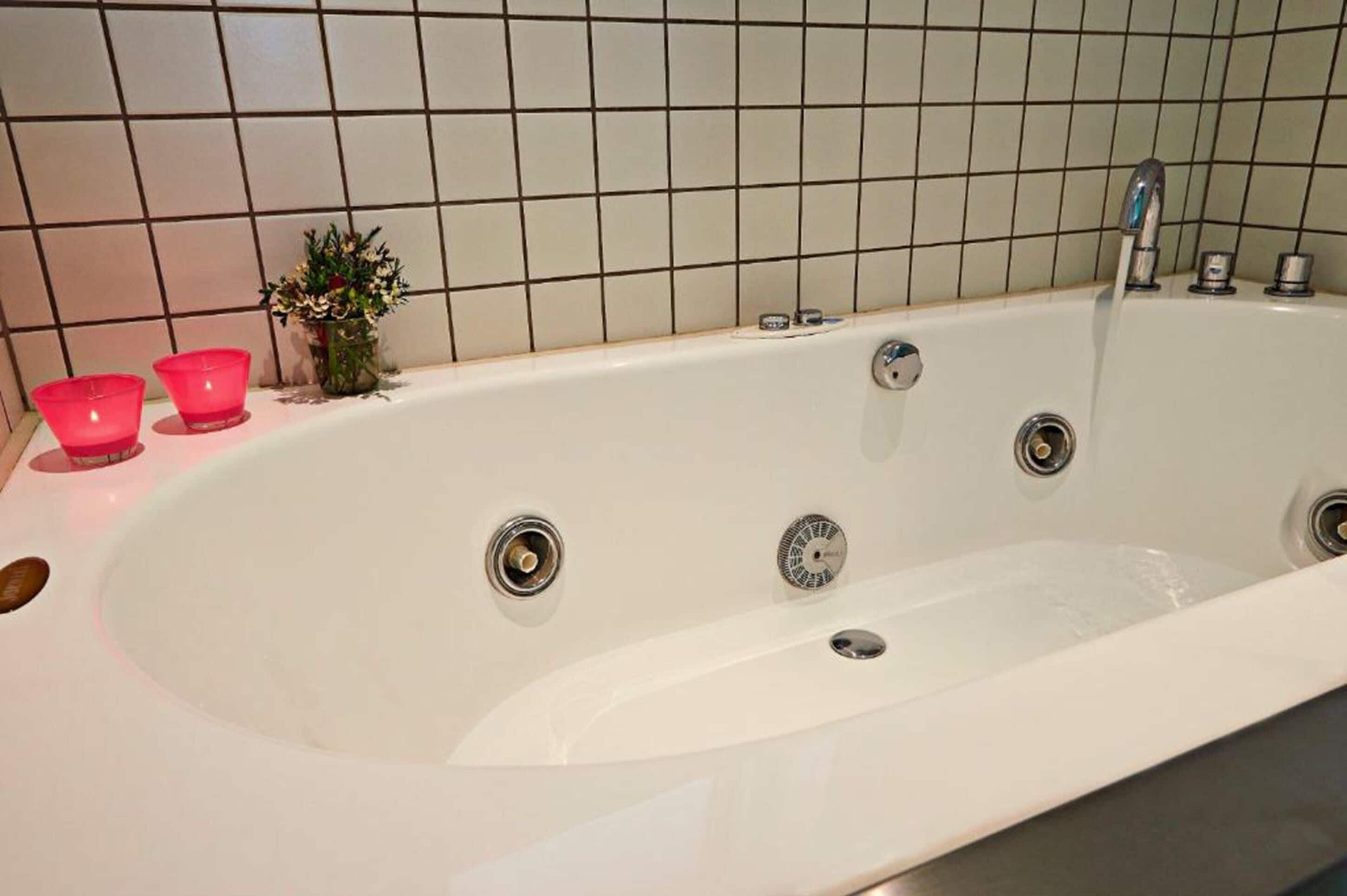 Una bañera blanca con un solo grifo y dos desagües, una planta pequeña y dos tazas rosas al lado.