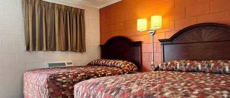 A hotel room with two beds, a brick wall, a window with curtains, and a wall-mounted lamp.