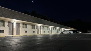 Um motel com uma fileira de quartos, cada um com porta e janelas. Há um carro estacionado no estacionamento.