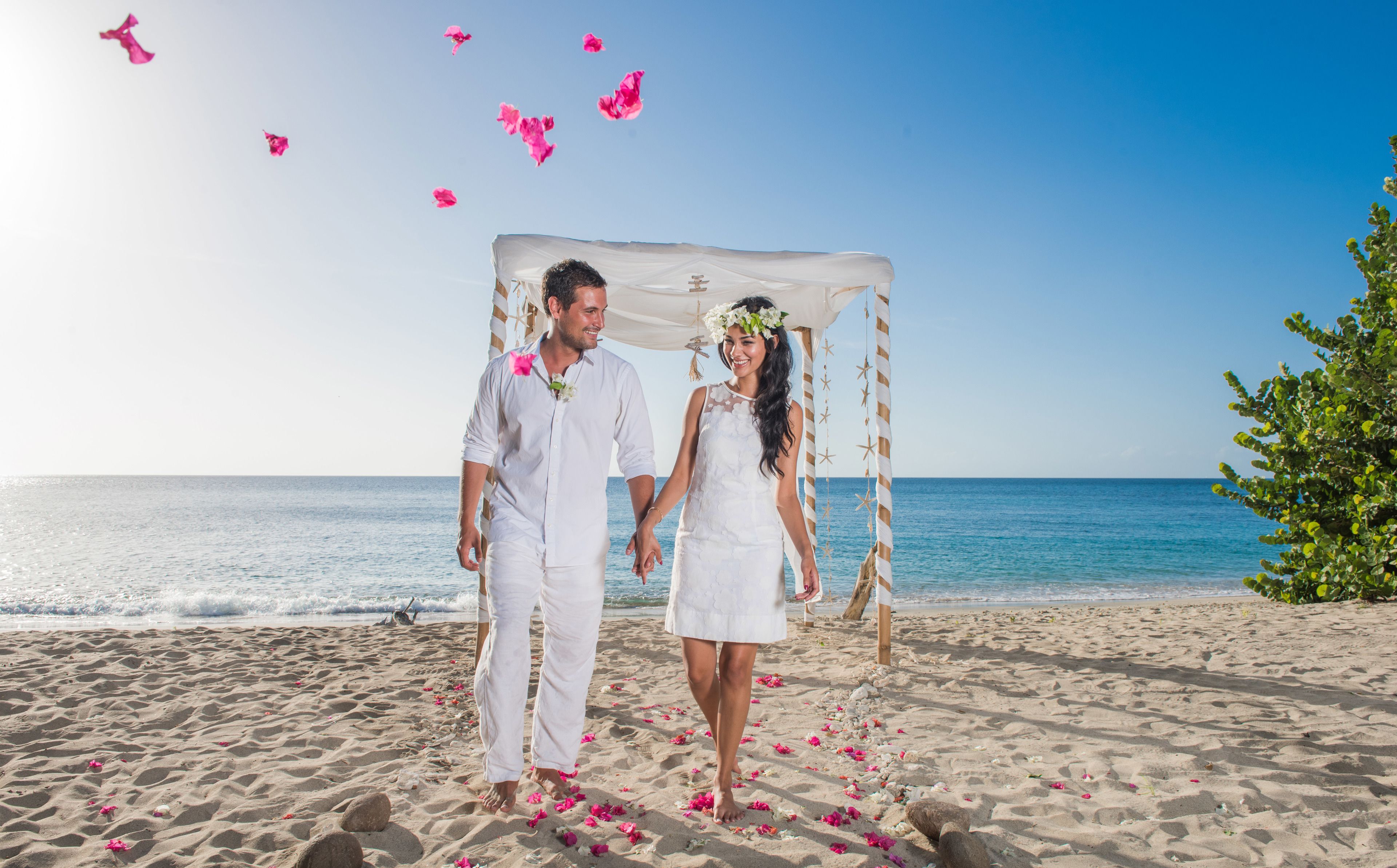 A couple walking on a beach with a white canopy and star decorations.