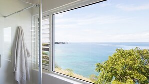 Une salle de bain avec une douche, un porte-serviettes et une fenêtre donnant sur la mer.