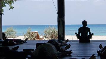 Un grupo de personas meditando en una terraza de madera con vista a una playa.