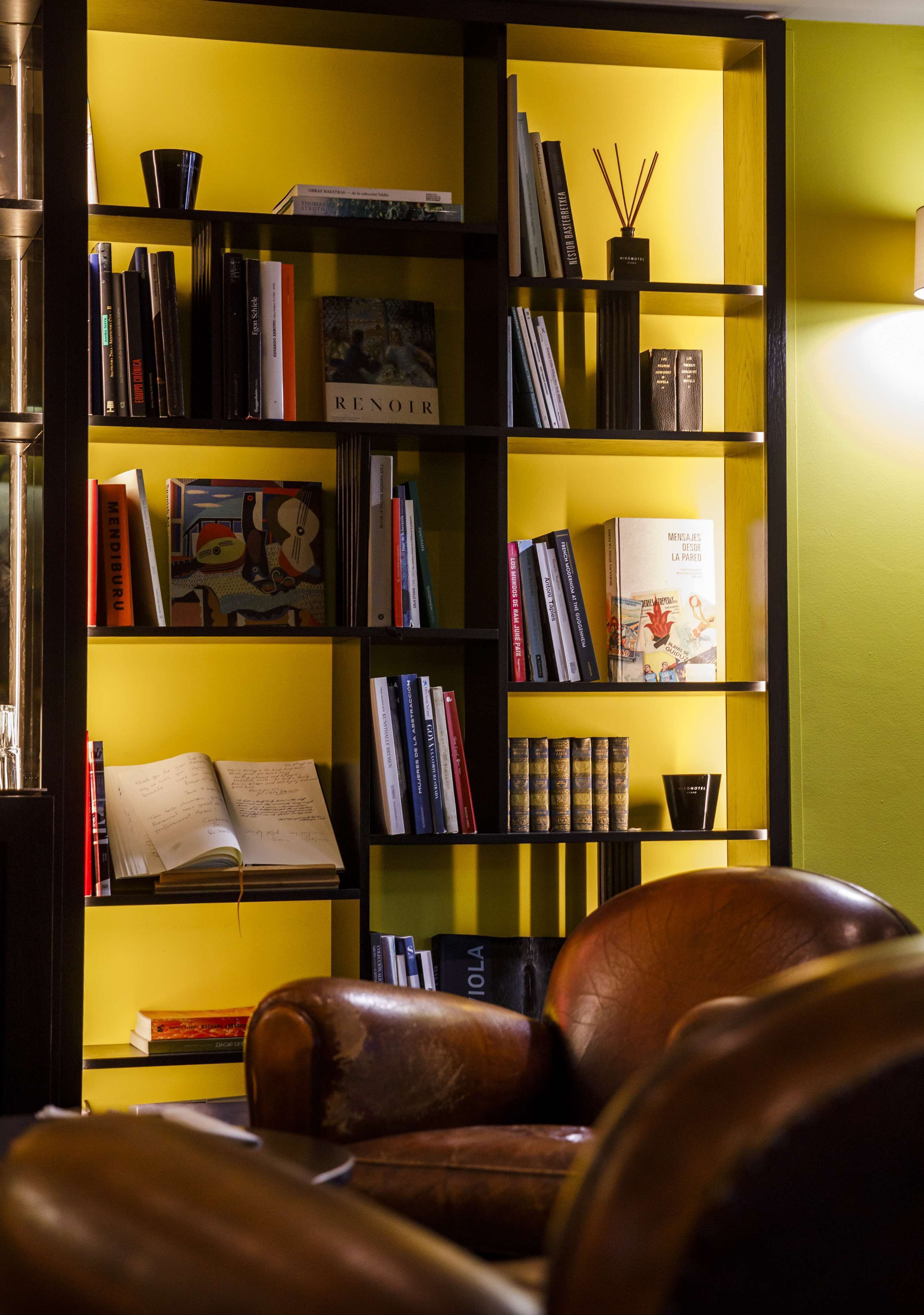 A room with a leather sofa, a bookshelf filled with books, a lamp, and a decorative vase.