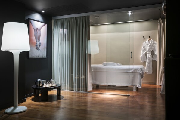 A modern bedroom with a bed, a bedside table, a lamp, a robe, and a large window with curtains.
