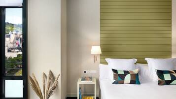 Habitación de hotel con cama, mesita de noche, lámpara y vistas al exterior.