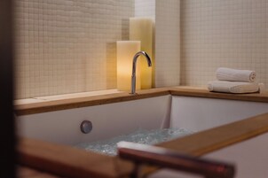 Ein Badezimmer mit einer Badewanne, einer Holzumrandung, einem Wasserhahn und einem Stapel Handtücher.
