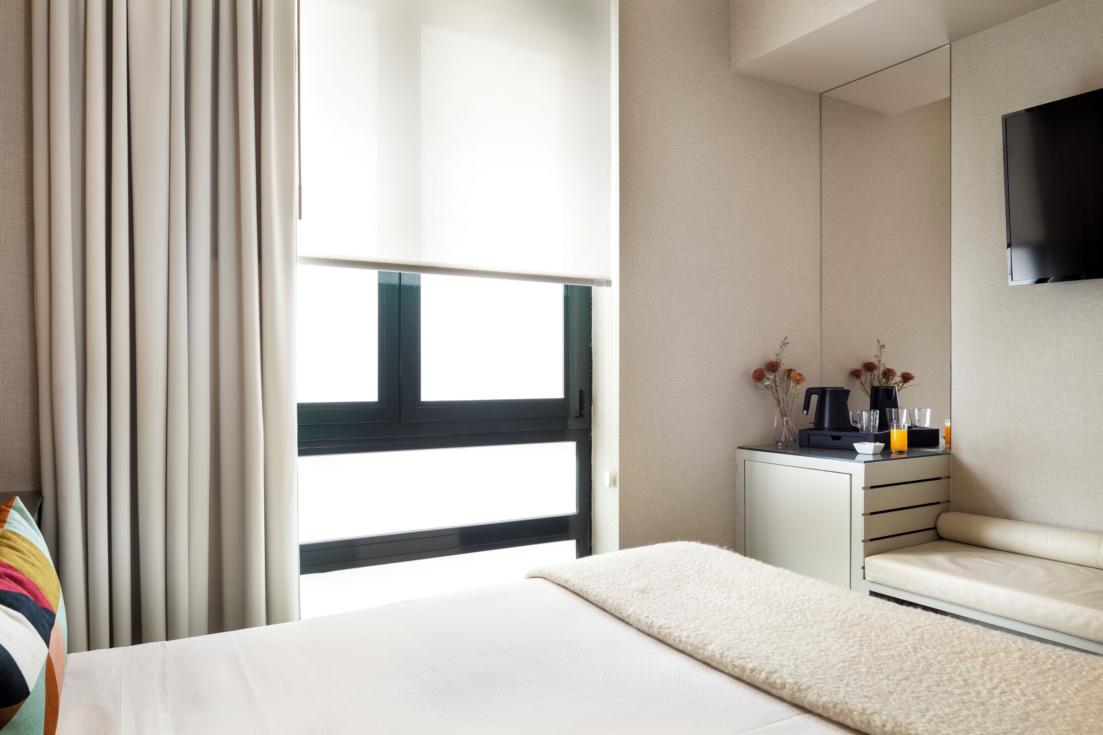 Ein modernes Hotelzimmer mit einem Bett, einer Sitzecke, einem kleinen Schreibtisch mit Kaffeemaschine und einem an der Wand montierten Fernseher.
